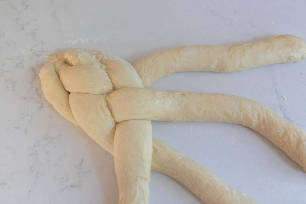braiding 4 strands of sourdough challah dough  on a white countertop 