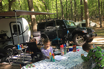 A boy and a girl site outside a camper enjoying a camping outing.