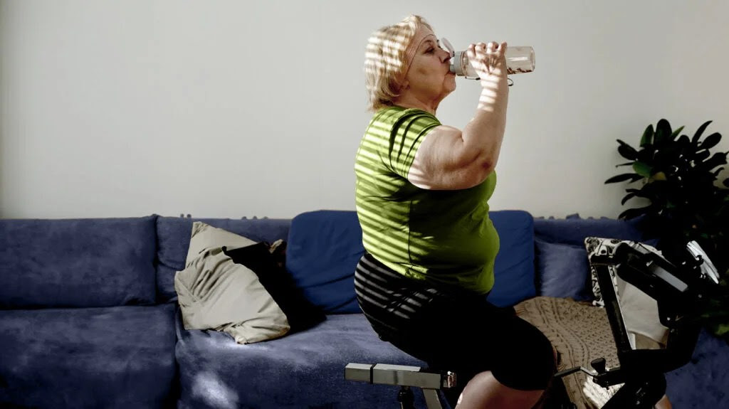 A woman on an exercise bicycle drinks water