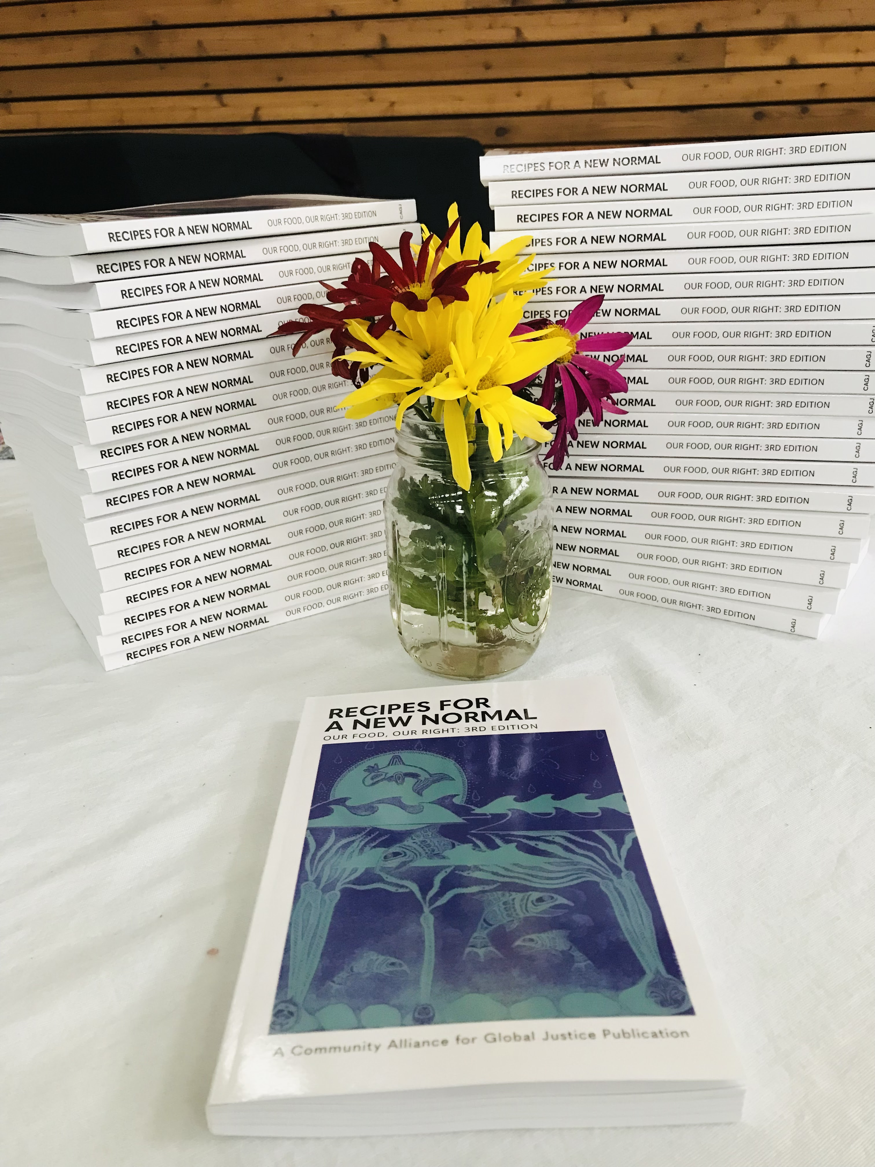 2 stacks of Our Food, Our Right: Recipes for a New Normal with a jar of flowers between them