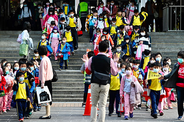 A large number of children wearing face masks descend the stairs of their elementary school