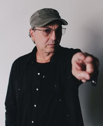 a man wearing glasses and a hat pointing at the camera