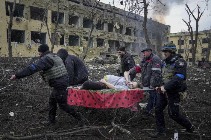 Ukrainian emergency workers carry an injured pregnant woman on a stretcher away from a maternity hospital damaged by shelling.