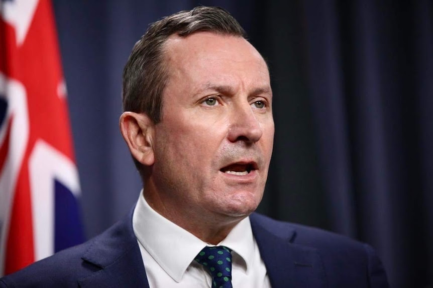 A man with short hair and a blue jacket delivers a speech at a lectern