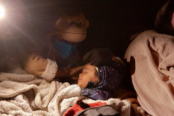 A woman wearing a hooded teddy bear jacket puts a child to sleep.