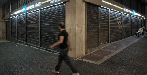 Un hombre camina delante de una sucursal cerrada del banco nacional de Grecia en Atenas./ EFE