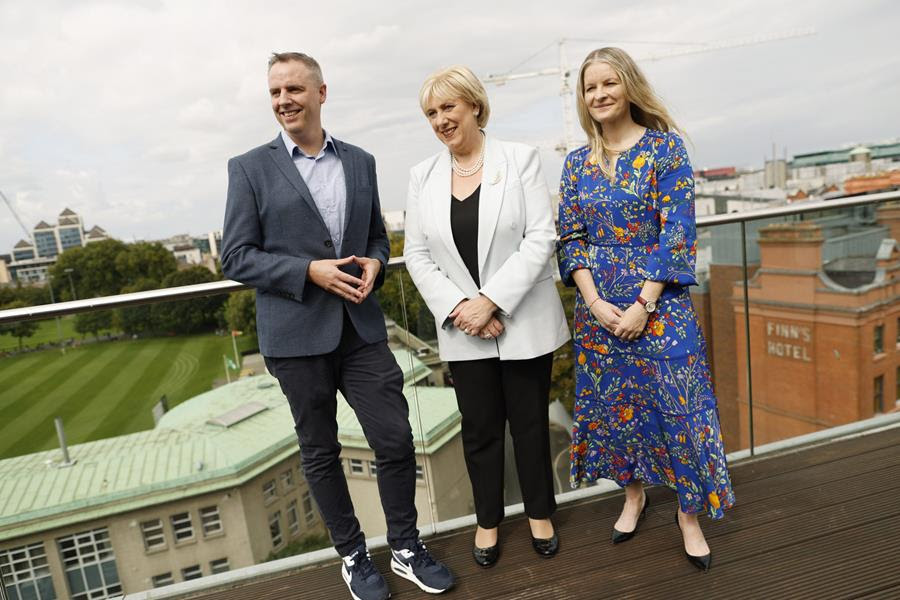 At the launch of the TikTok Digital Future Fund are (L-R) Cormac Keenan, Head of Trust & Safety, TikTok; Minister Heather Humphreys TD, Minister for Rural and Community Development and Minister for Social Protection; Áine Kerr, Chair of the Board, Rethink Ireland. They are standing on a balcony and looking off into the distance with a smile.