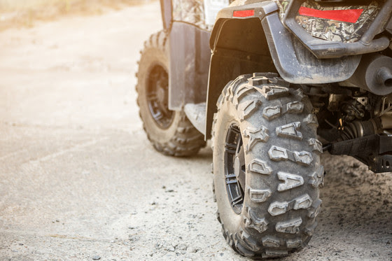 Close-up tail view of the back of an ATV-quad-bike. All that is visible is a muddy tire and part of the back of the vehicle.