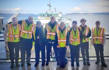 Group of eight people in safety vests posing for a photo at a ferry terminal