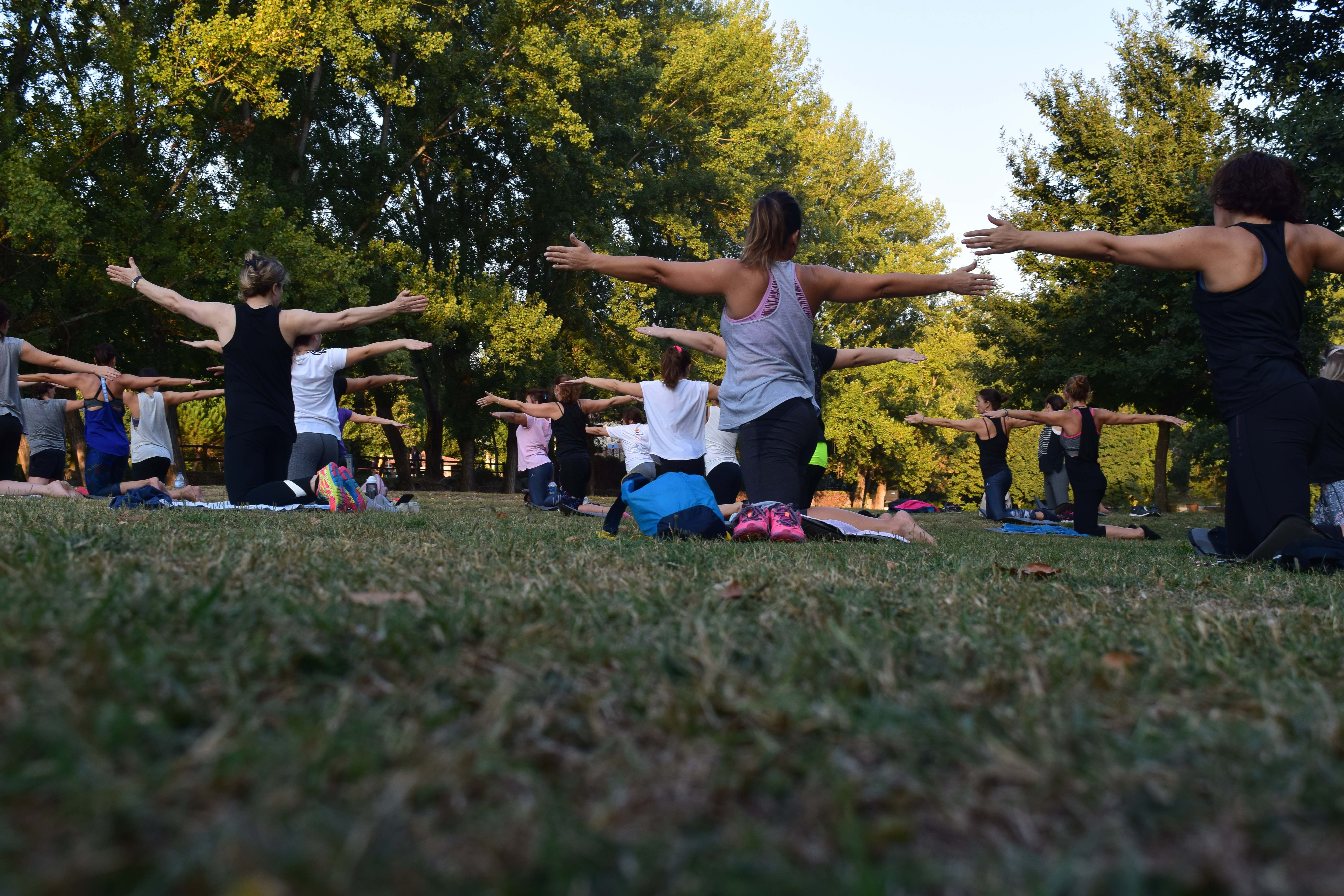 Group of people with arms outstretched doing yoga in a park.