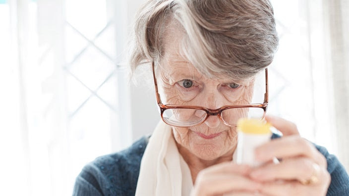 An older woman examining a pill bottle closely.