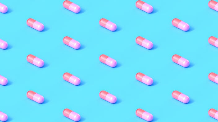 Red and pink capsule pills lined up in a diagonal pattern on a light blue background.