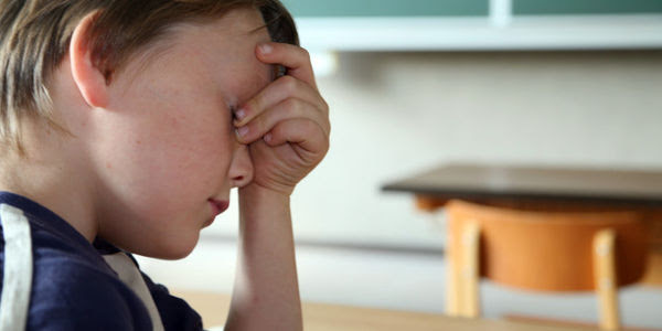 A child sits at a school desk, head in hand.