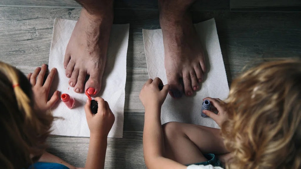 Two blond children painting a grownup's toenails in bright colors