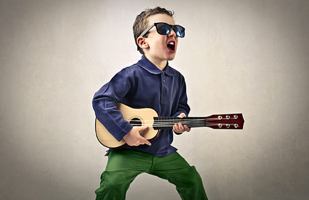 A little boy singing and playing the guitar with sunglasses on.