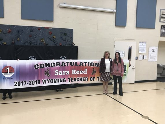 State Superintendent Jillian Balow and Sara Reed stand in front of a large banner that reads, "Congratulations Sara Reed, 2017-2018 Wyoming Teacher of the Year"