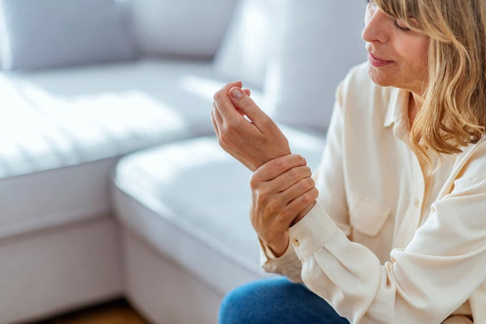 Cropped shot of a woman rubbing her wrist from joint pain. She is sitting on her couch in the living room.