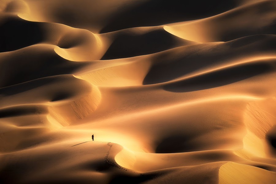 A lone figure is seen standing atop a vast series of sand dunes.