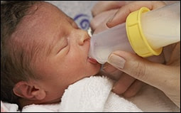 The figure shows a newborn being fed with a bottle.