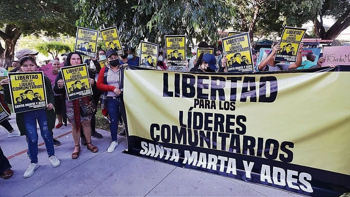a crowd of people gather holding a banner and several posters calling for the release of the five environmental defenders from Santa Marta.