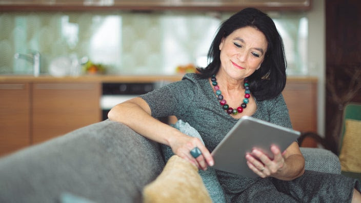 A woman with long, dark hair is using a tablet to look something up at home.