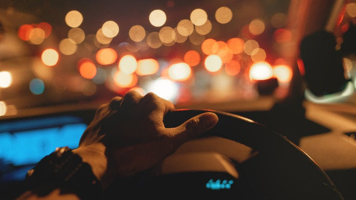 A close-up image shows a hand on a steering wheel at night.