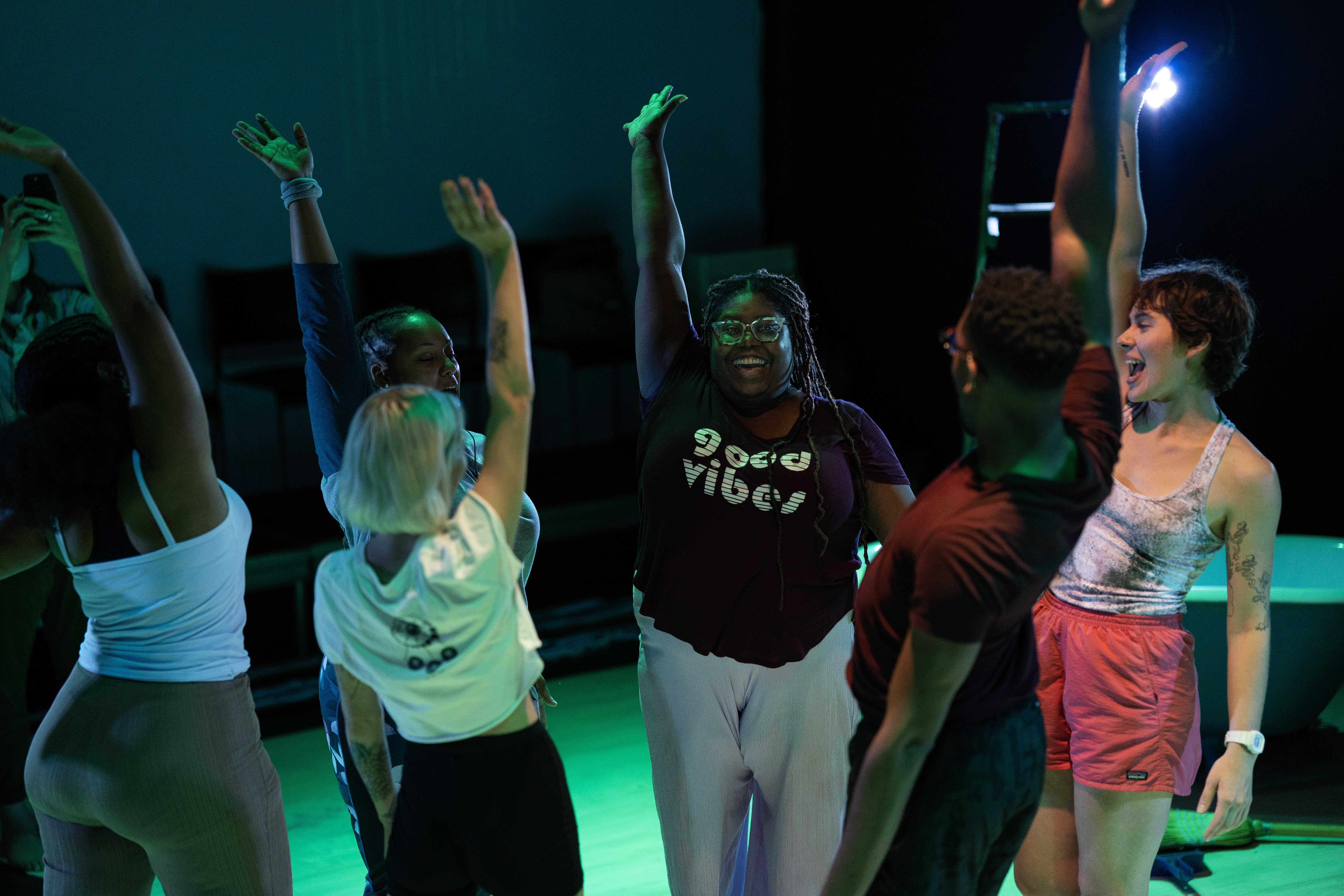 A group of people on stage standing in a circle raising their arms in excitement.