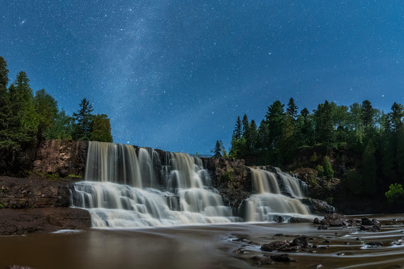 Waterfalls under a starry sky framed by evergreens