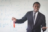 black male teacher with formulas on white board behind him
