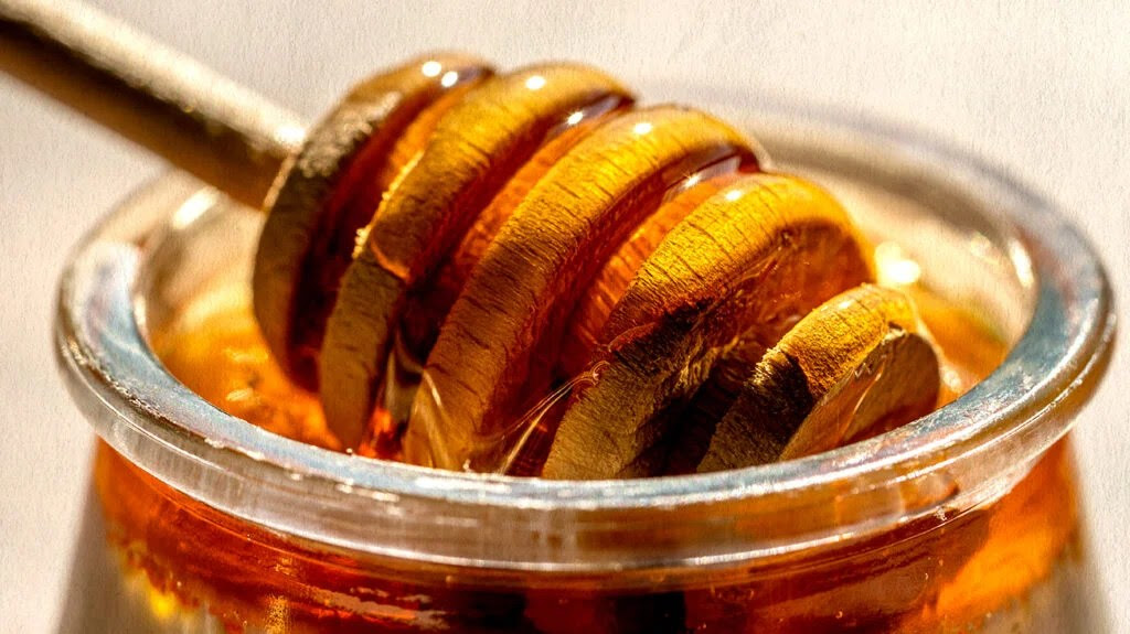 A close up shot of a jar of honey and a honey dipper