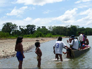 Un bote con personas de la zona se detiene junto a la orilla del río cerca de los mashco-piros. Los niños mashco-piros visten con ropa que les han dado.