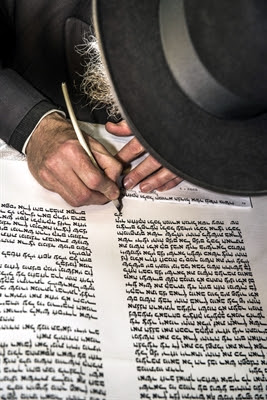 An Orthodox Jewish man writes
                  a Torah scroll.