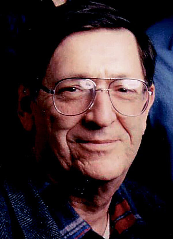 A close-up portrait of Warren Boroson, smiling, wearing wire-rimmed glasses.