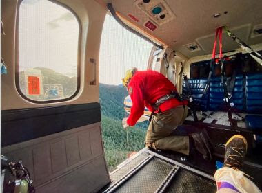 Forest Ranger leans out of helicopter during hoist rescue