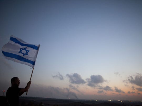 A man stands with an Israeli flag on a hill overlooking the Gaza Strip on July 20, 2014. (Photo by Lior Mizrahi, Getty Images)