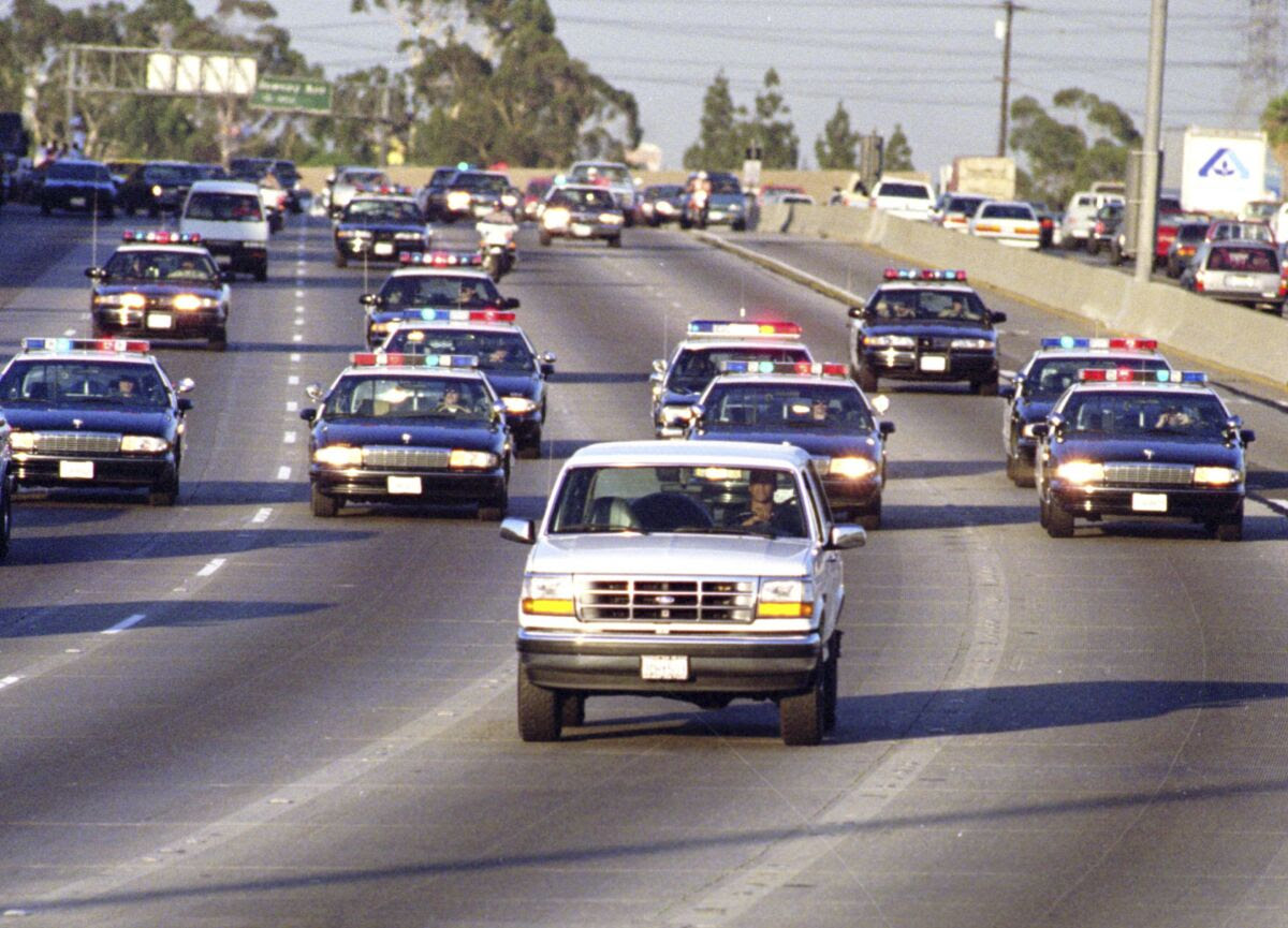 A white SUV is followed by at least a dozen police cars in a highway