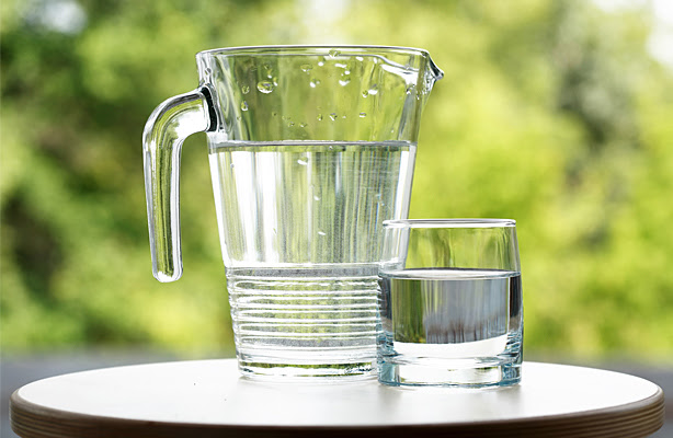A pitcher and glass of water sitting on a table outside.