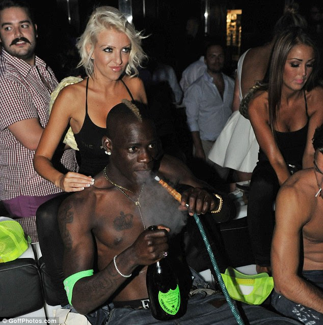 Party time: Mario Balotelli smokes a hookah pipe while holding a bottle of champagne as he receives a massage
