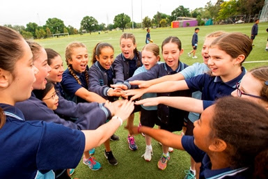 Children stand in a circle on a sporting oval.