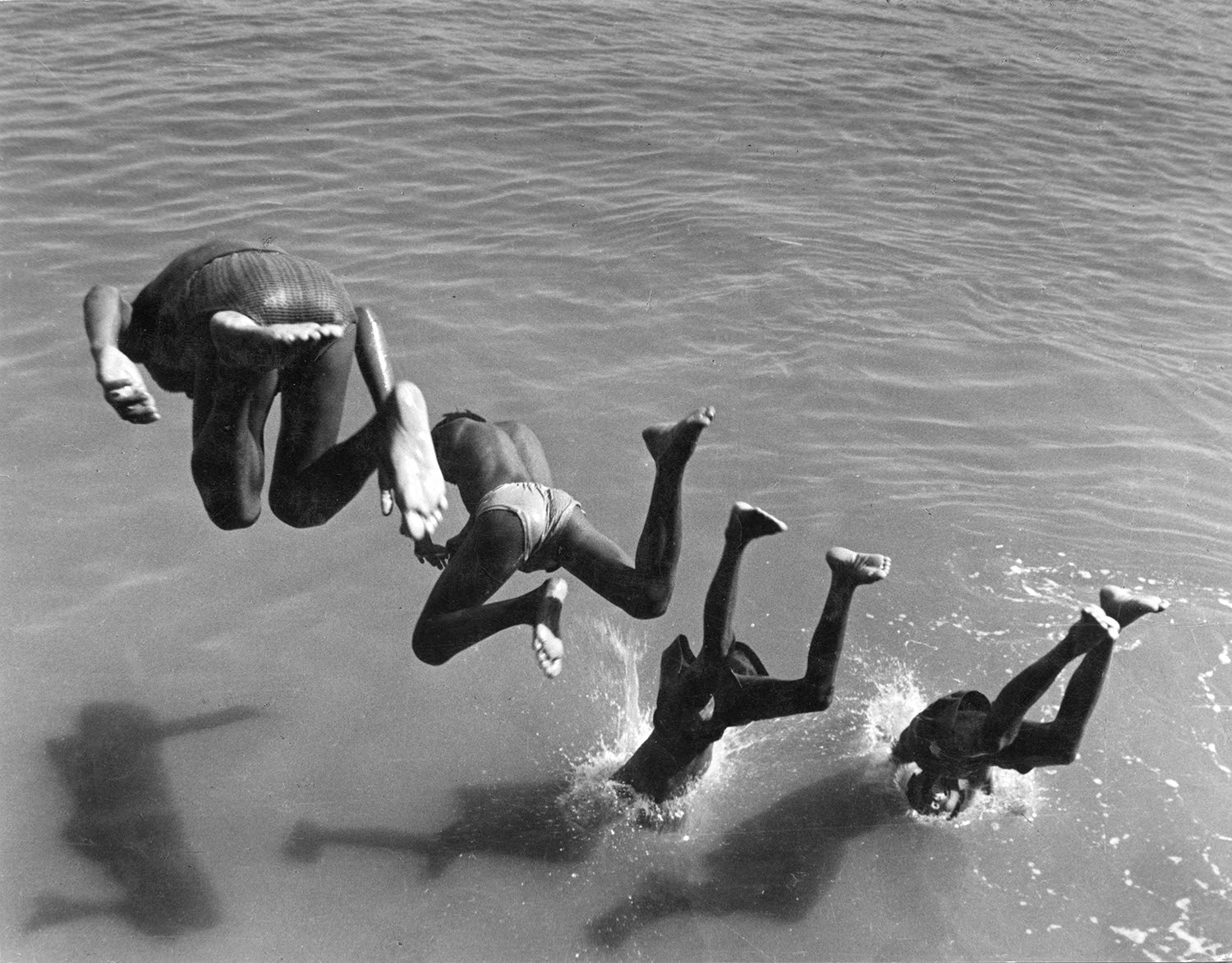 Four boys diving in the water in an order.