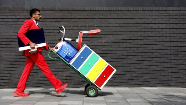 Foto mostra homem empurrando um arquivo e uma cadeira em um carrinho de mão