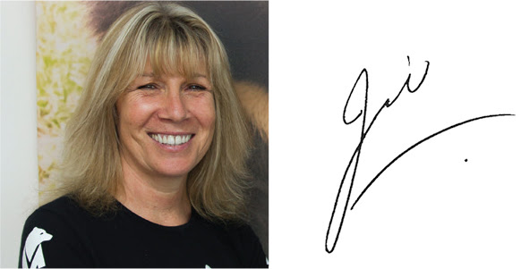 Een close-up headshot van de oprichter en CEO van Animals Asia, Jill Robinson, glimlachend in de camera met blond schouderlang haar. Ze draagt een zwart t-shirt met het witte Animals Asia-logo op haar hemdsmouw.