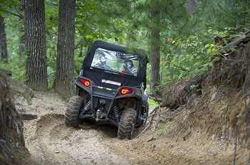 a black, topped off-road vehicle leaves ruts in the dirt as it climbs up a sloped trail surrounded by mature trees