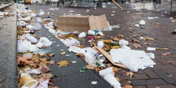 A sidewalk is covered in crushed used coffee cups, plastic bags, takeout containers, boxes, and beverage cans.