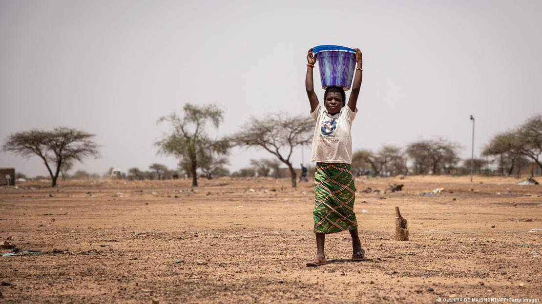 Mulher carrega balde d'água na cabeça em paisagem árida