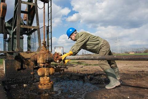 An engineer inspects a valve on an oil pump.