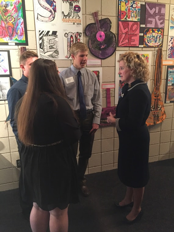 Superintendent Balow visits with three high school students in the lobby of the Cheyenne Civic Center, where student art is displayed on the wall.