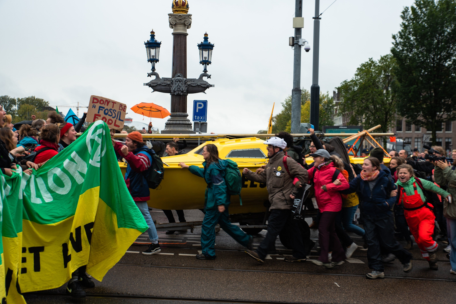 Around 20 rebels marching along a bridge, surrounding a yellow boat which they are pushing along with them.