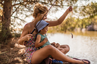 mom and son sitting on riverbank holding fish on line