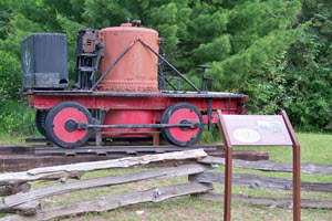 An old steam locomotive sits on an outdoor platform. An interpretive sign is in front of it.